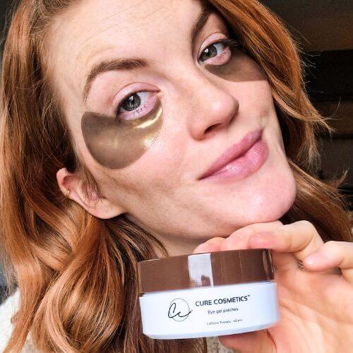 Kvinne med Caffeine Therapy øyemasker fra Cure Cosmetics som reduserer mørke ringer og gir huden under øynene frisk glød.
