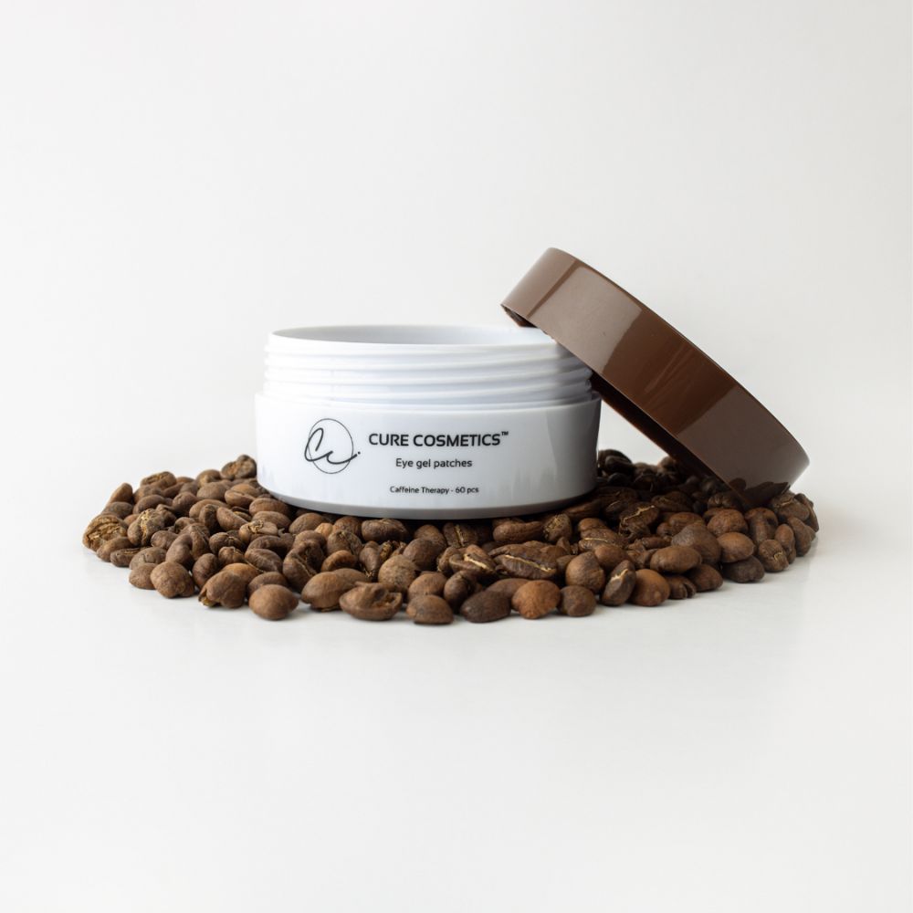 Åpen boks med Caffeine Therapy øyemasker fra Cure Cosmetics omgitt av kaffebønner – hydrogel eye patches med koffein som reduserer mørke ringer og gir glød under øynene.