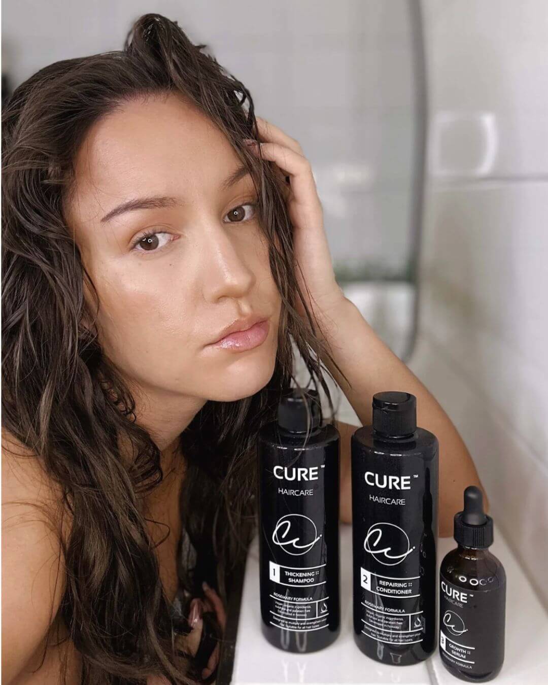 Kvinne med vått hår bruker Rosemary Therapy hårpleiesett fra Cure Cosmetics med shampoo, conditioner og serum for tykkere og sunnere hår.