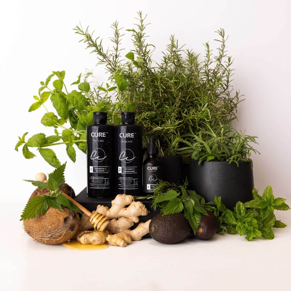 Rosemary Therapy hårpleiesett fra Cure Cosmetics omgitt av naturlige ingredienser som rosmarin, ingefær, kokos, honning og avokado.