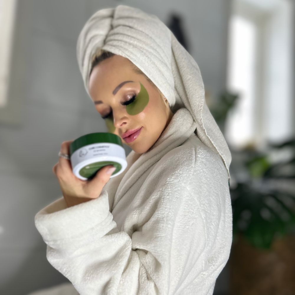 Kvinne med Seaweed Therapy øyemasker fra Cure Cosmetics nyter egenpleie i morgenkåpe – reduserer poser og rynker under øynene.