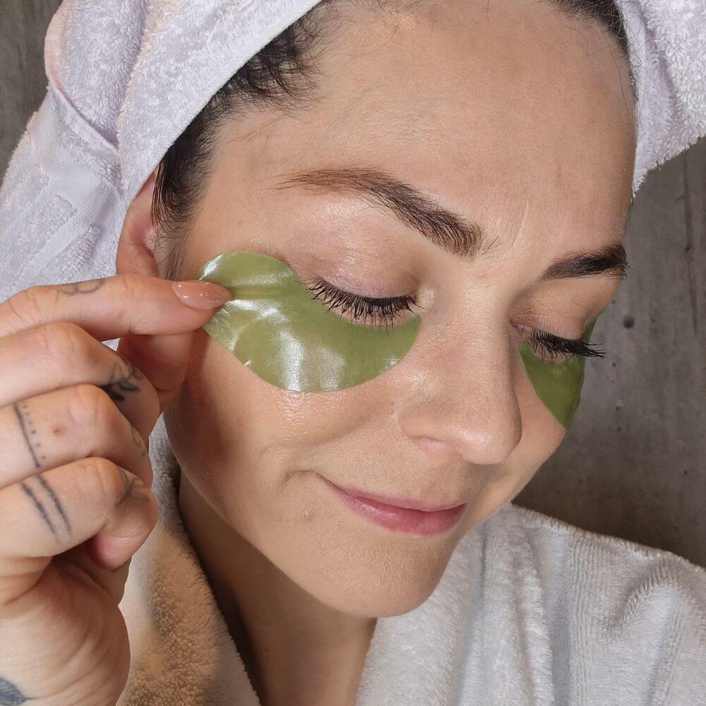 Kvinne påfører Seaweed Therapy øyemasker fra Cure Cosmetics for å redusere poser og rynker under øynene.